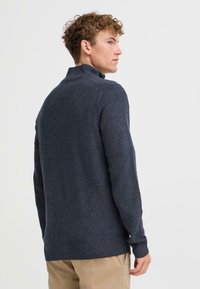 Jersey de punto azul marino oscuro con cuello alto, puños y dobladillo acanalados; tejido texturizado con un diseño ajustado.