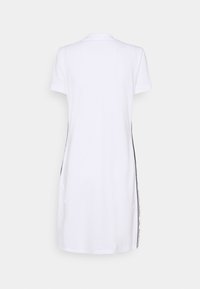 Vit poloklänning med korta ärmar, med svarta sidodetaljer och en mjuk yta. Enkelt design med klassisk krage.