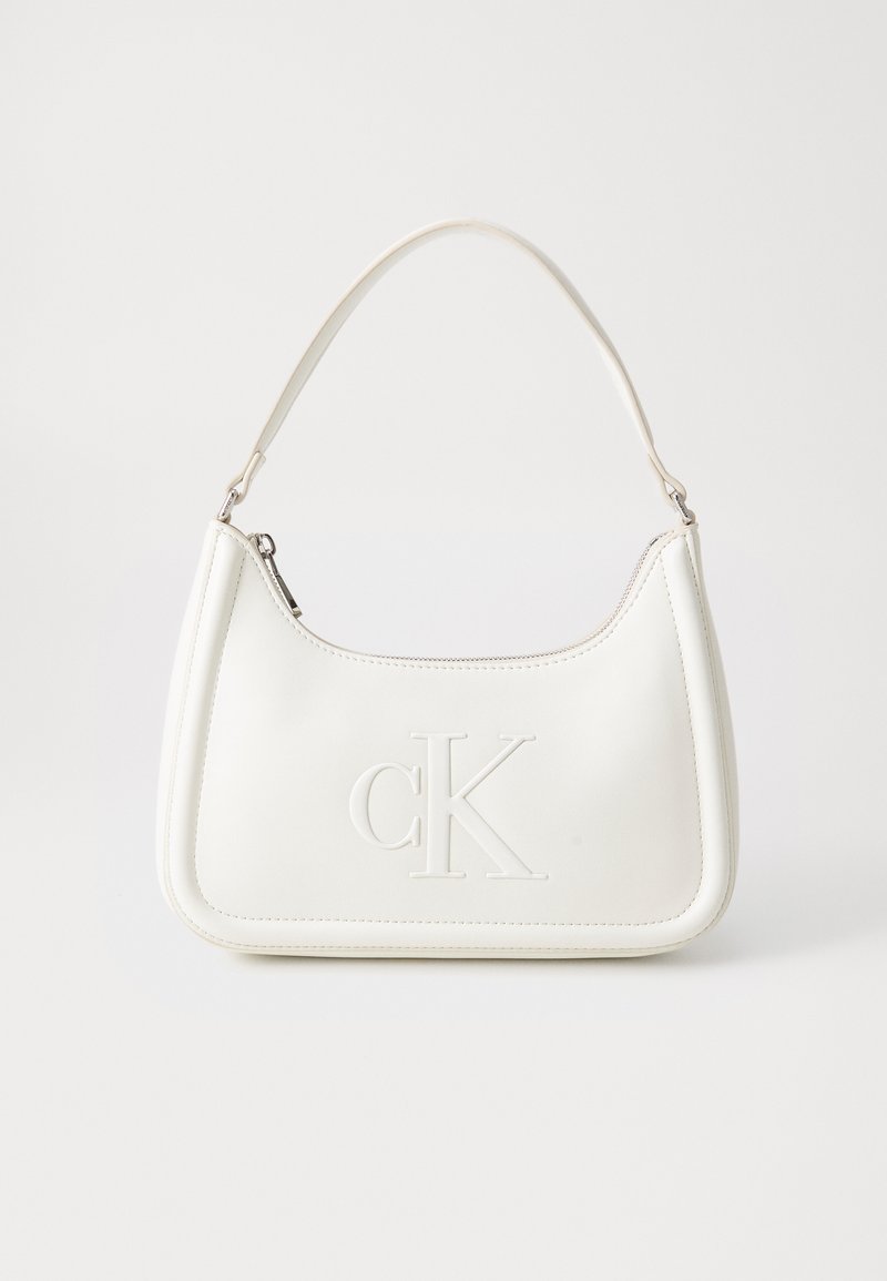 Valge nahast käekott, millel on kumer kuju, esiküljel on reljeefne "CK" logo ja üks õlavarre rihm. Ülemine tõmblukkuu.