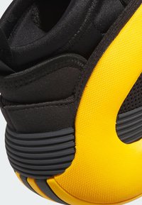 Zwarte en gele sportieve schoen met een gedetailleerde rubberen hak, een bovenwerk van mesh en een kenmerkend cirkelvormig uitsnijdingsontwerp.