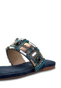 Sandalia plana azul con una amplia tira decorada con rhinestones plateados, negros y turquesas, con una suela suave y lisa y un diseño minimalista.
