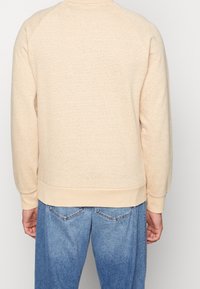 Felpa a maglia beige chiaro con collo rotondo a costine, maniche lunghe e vita a costine. Il tessuto testurizzato presenta strisce orizzontali.