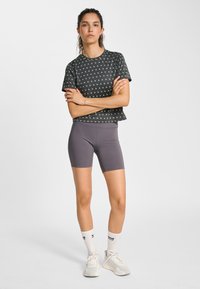 Svart t-shirt med kort ärm och grönt mönster, kombinerad med gråa cykelshorts. Vita ankelstrumpor och ljusgrå träningsskor fulländar looken.