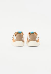 Baskets avec une combinaison de suède orange et d'accents beiges, comportant un logo blanc, une languette bleue et une semelle en caoutchouc texturé.