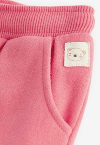 Roze gebreide sweatpants met een geribde tailleband, zijzakken en een vierkante patch met een berenillustratie. Zacht en gestructureerd materiaal.
