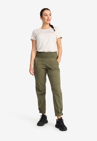 Olive green cargo pants with elastic waistband, zip pockets, and adjustable cuffs, paired with a light grey T-shirt and black sneakers.