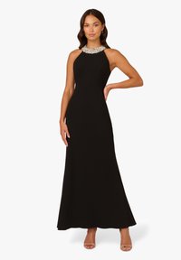 Schwarzes Abendkleid mit einem figurbetonten Oberteil, halterlosen Ausschnitt besetzt mit Juwelen und einem ausgestellten Saum. Glattes Material mit leichtem Glanz.