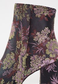 Bottine en tissu avec un motif floral dans des tons de violet, vert et bordeaux sur fond noir. Texture lisse et forme structurée.