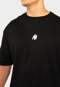 T-shirt noir en coton, ornée d'un petit graphisme de gorille blanc sur la poitrine. Manches courtes et col rond. Texture lisse.