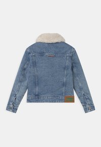 Denimová bunda ve světle modré barvě s límcem z umělé kožešiny, má knoflíkové manžety a nášivku s nápisem "TOMMY HILFIGER" v zelené barvě na spodním lemu.