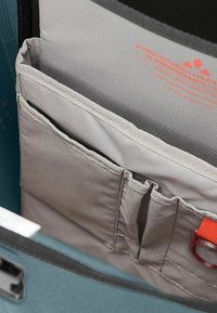 Poches en tissu gris avec des bords renforcés à l'intérieur d'un sac teal, présentant des accessoires rouges et un texte indiquant des matériaux imperméables et durables.