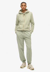 Jasnozielona bluza z kapturem z zamkiem z przodu i sznurkiem, w komplecie z dopasowanymi dresami. Miękki materiał, elastyczne mankiety i kieszenie.