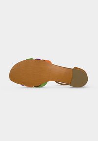 Sandale avec semelle plate marron et petit talon, brides multicolores visibles en vert, violet et orange, vue de dessous sur fond blanc.