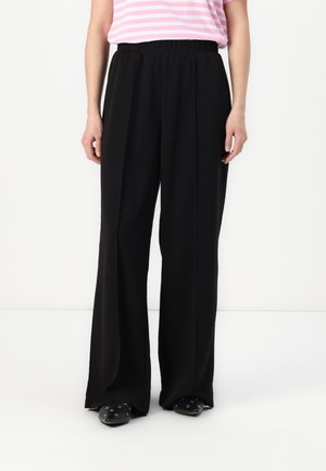 Pantalons larges noirs en tissu léger avec une taille élastique, associés à un haut rayé rose et blanc.