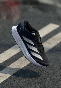 Black athletic shoe with white stripes, lightweight mesh upper, textured sole, and a cushioned design, displayed mid-air against a gray background.