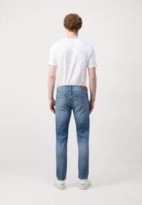 Lichtblauwe denim jeans met een rechte snit, vijf zakken en een bruine leren patch op de tailleband. gedragen met een wit T-shirt.