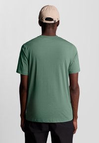 T-shirt verde a maniche corte realizzata in tessuto morbido, con scollatura rotonda e design minimalista. Indossata con un cappellino beige.