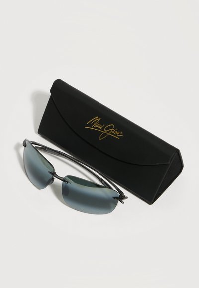 Γυαλιά ηλίου χωρίς σκελετό με μπλε φακούς δίπλα σε μια μαύρη ορθογώνια θήκη με χρυσό λογότυπο Maui Jim σε λευκό φόντο.