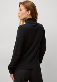 Maglione nero lavorato a maglia con colletto alto, maniche lunghe e orlo a coste. Texture liscia con una silhouette aderente. Design minimalista.