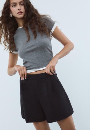 Grå ribbade kortärmade topp med vit krage, ihop med högmidjade svarta veckade shorts. Slät textur och skräddarsydd design.