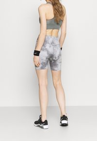 Šedé batikované šortky z elastické látky, doplněné šedou sportovní podprsenkou. Atletický vzhled zdůrazňují černé zápěstní pásky a tenisky.