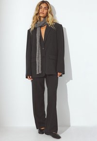 Stribet sort jakkesæt med brede bukser og en oversized blazer, parret med et gråt tørklæde og sorte flade sko. Glat tekstur og skræddersyet pasform.