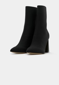 Paire de bottines noires à talons blocs et bouts pointus sur fond blanc.