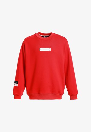 Sudadera roja de mangas largas, con escote redondeado, que presenta un parche rectangular blanco en el frente y un acento de etiqueta negra en la manga.