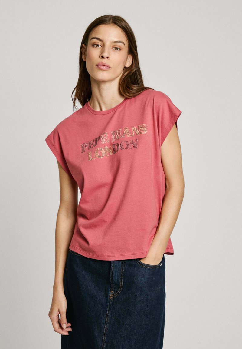 Rožinė medvilninė marškinė su suktomis rankovėmis, ant kurių užrašyta "PEPE JEANS LONDON" metalizuota auksine spalva, derinama su tamsiai mėlynomis džinsinėmis sijoninėmis.