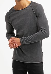 Chemise à manches longues gris foncé, texture côtelée, décolleté rond avec des coutures contrastantes, design ajusté, associée à un pantalon noir.