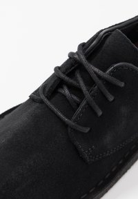 Black suede lace-up shoe with textured surface, accented stitching, and matching black laces. Features a traditional design.