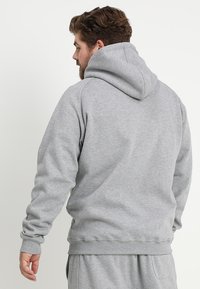Sudadera gris con una capucha grande, puños y dobladillo acanalados. El material parece suave con un acabado ligeramente texturizado. Sin logos ni patrones visibles.