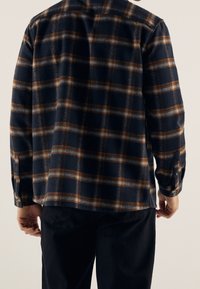 Laivastonsininen flanellipaita, jossa on ruskea ja vaaleansininen ruutukuosi, pitkät hihat ja napilliset kalvosimet, valmistettu pehmeästä kankaasta.