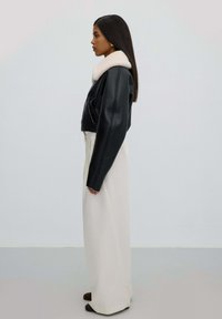 Zwarte leren cropped jas met een witte bontkraag, gecombineerd met witte wijde broekspijpen. Eenvoudig ontwerp en gladde texturen.