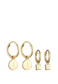 Pendientes de aro en tono dorado con un charm circular marcado como "925" y un par más pequeño con un charm en forma de tostada. Textura metálica suave.
