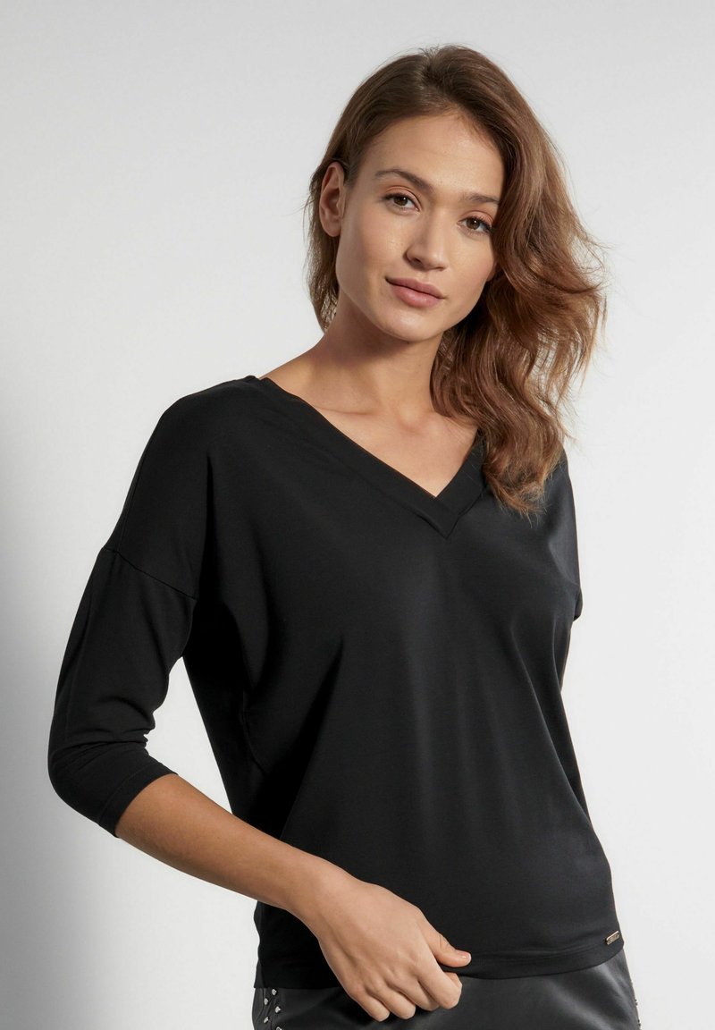 Czarny top z dekoltem w serek i rękawami o długości 3/4, wykonany z gładkiej tkaniny. Charakteryzuje się luźnym krojem i subtelnym logo na brzegu.