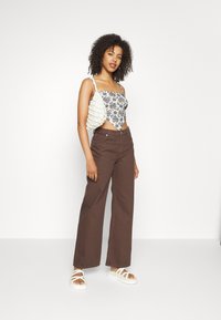 Fato justo com padrão floral em azul claro e branco, combinado com calças largas castanhas. Acessórios incluem uma bolsa texturizada branca e sandálias.