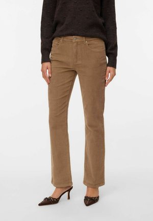 Persona que lleva pantalones marrones de pana de pernera recta, suéter texturizado marrón oscuro y mocasines marrones de tacón con punta y detalles de ojales.