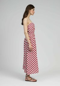 Robe maxi sans bretelles rouge et blanche à rayures, avec un corsage ajusté, une taille froncée et un ourlet fluide, assortie à des sandales plates brunes.