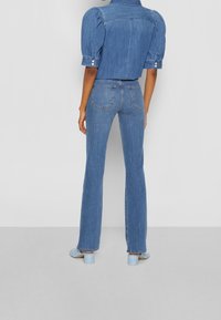 Conjunto de denim con una blusa ajustada de mangas abullonadas y unos vaqueros de talle alto y campana en azul medio. Textura suave con detalles de costura clara.