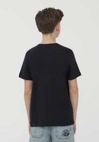 T-shirt nera a maniche corte con scollatura rotonda, texture liscia e vestibilità morbida, mostrata da dietro, abbinata a pantaloni corti in denim chiaro.