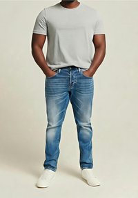 Camiseta de manga corta gris, vaqueros azules de mezclilla con detalles desgastados, y zapatillas blancas. La camiseta tiene un cuello redondo; los vaqueros cuentan con cinco bolsillos.