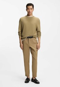 Maglione kaki lavorato a maglia con scollo rotondo, abbinato a pantaloni color cuoio a gamba stretta e scarpe di pelle nere, caratterizzato da una texture liscia e motivi sottili.