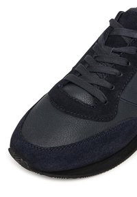 Sötétkék sneaker sima bőrből és velúrból, kerek orral, texturált fűzőkkel és kontrasztos varrási részletekkel.