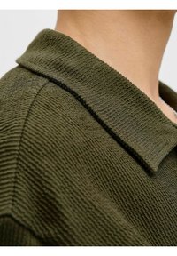 Polo shirt vert olive texturé avec un col côtelé, mettant en valeur un tissu tissé et une vue rapprochée de la couture de l'épaule.