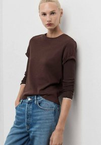Bruine katoenen t-shirt met opgerolde mouwen, ronde halslijn en een relaxte pasvorm, gecombineerd met lichtblauwe high-waisted jeans. Effen textuur.