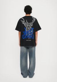Svart oversized t-skjorte med hvit og blå grafikktrykk som viser en hjort og tekst. Kombinert med løstsittende, falmede blå denimjeans.