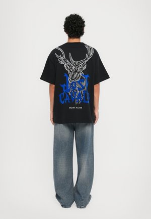 Camiseta negra de gran tamaño con estampado gráfico en blanco y azul que representa un ciervo y texto. Combinada con unos jeans vaqueros de denim azul claro y holgados.
