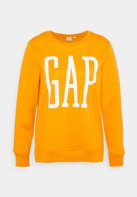Oranžová mikina vyrobená z měkké tkaniny s kulatým výstřihem. Na přední straně se nachází velké bílé logo "GAP" umístěné na středu. Ribovaná manžeta a lem.