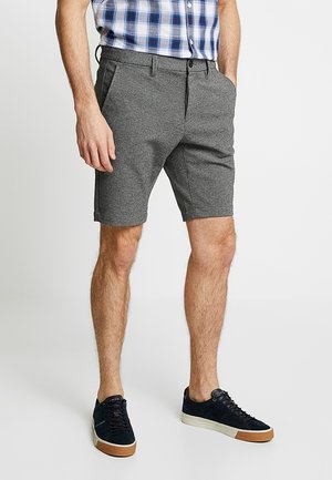 Graue, maßgeschneiderte Shorts mit glatter Textur, Seitentaschen und einer Länge bis zur Mitte des Oberschenkels, kombiniert mit marineblauen Sneakers und einem karierten Hemd.